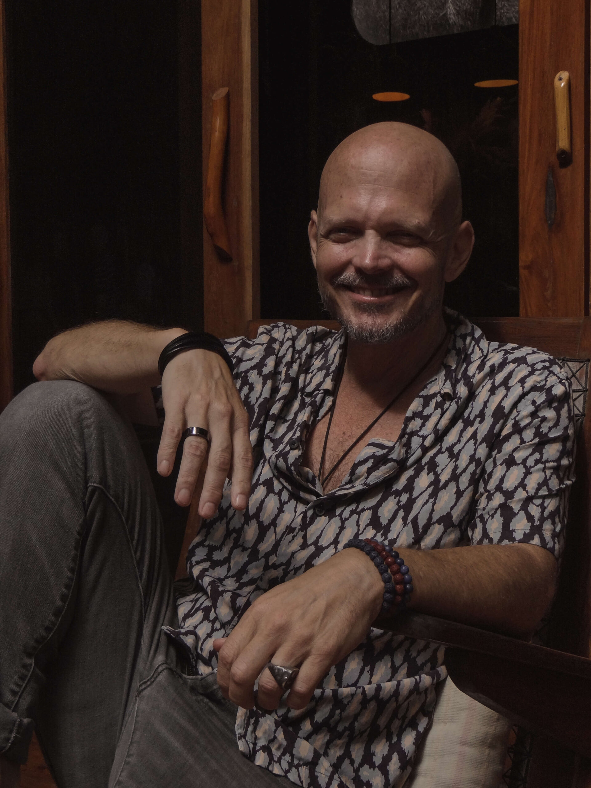 Brian Begin A bald man with a beard sits relaxed in a chair, smiling. He is wearing a patterned shirt and multiple rings and bracelets, exuding an aura of personal growth. As if ready to delve into spirituality, he radiates calmness akin to a guest on the Brian Begin Podcast. Brian Begin Podcast