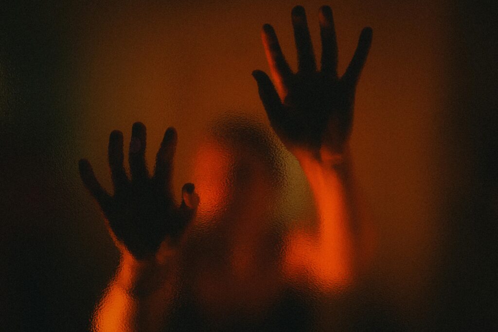 Brian Begin A blurry silhouette of a person with both hands pressed against a textured, semi-opaque glass, illuminated by warm orange light. Brian Begin Podcast