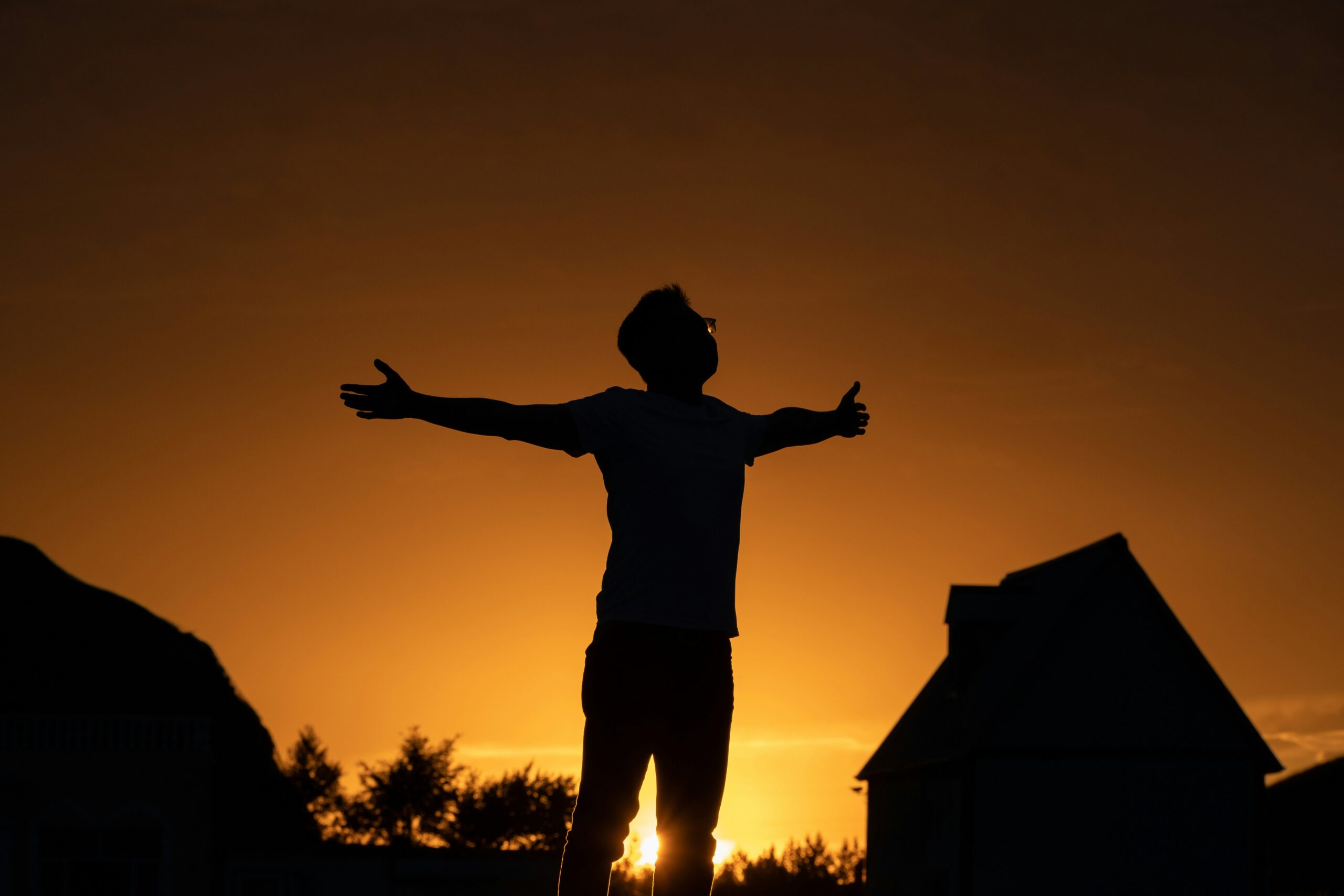 Brian Begin Silhouette of a person standing outdoors with arms outstretched at sunset, with buildings and trees in the background. Brian Begin Podcast
