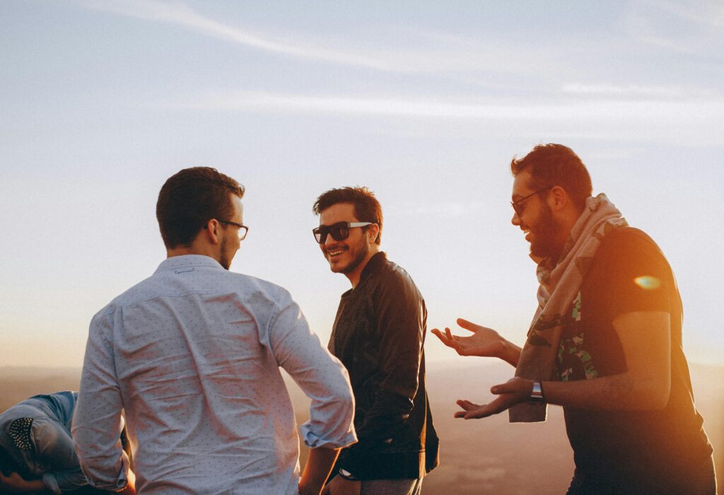 Brian Begin Three men wearing sunglasses and casual clothes stand outdoors at sunset, talking and laughing together. Brian Begin Podcast