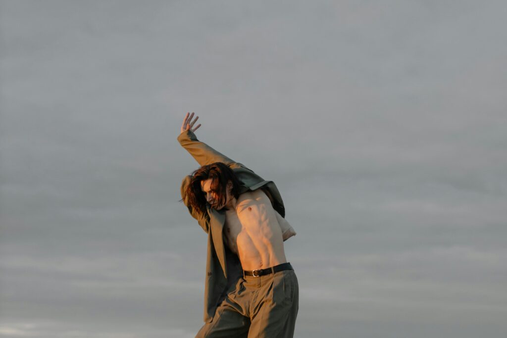 Brian Begin A person wearing an open jacket and pants stands outdoors under a cloudy sky, raising one arm and partially exposing their torso. Brian Begin Podcast
