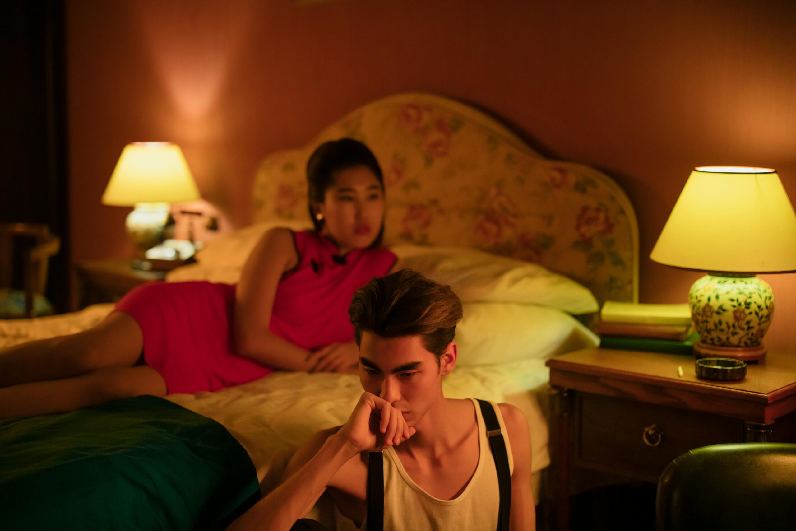 Brian Begin A man sits pensively on the edge of a bed while a woman in a red dress reclines behind him. The room is dimly lit by two bedside lamps. Brian Begin Podcast