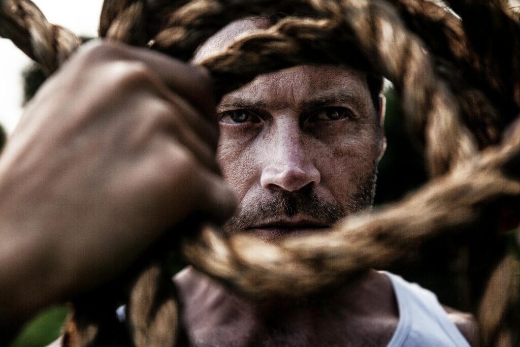Brian Begin A man wearing a white tank top looks intently through a coiled rope held in front of his face. Brian Begin Podcast