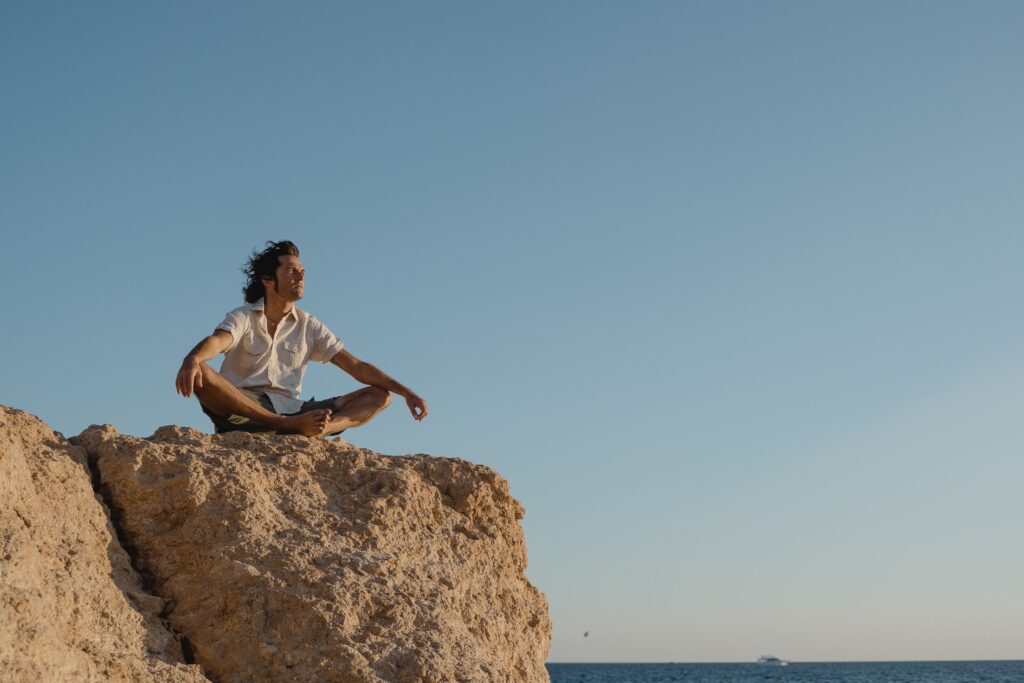 Man sitting peacefully in nature representing inner peace, self-sourced confidence, and detachment from external outcomes"